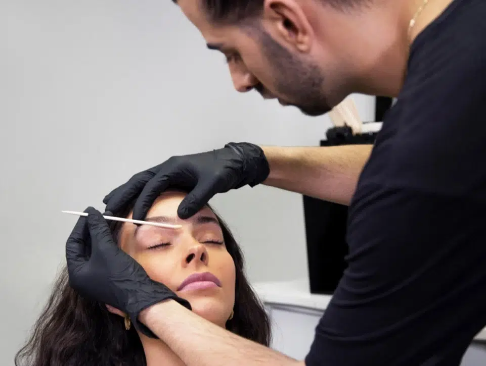 a beauty technician shaping a women's eyebrows